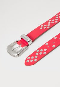 Cintura rossa in gomma con dettagli in metallo argentato. Presenta una fibbia rettangolare in metallo argentato con bordo strutturato. Design piatto e texture liscia.