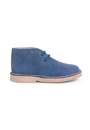 Botas de tobillo de ante azul con dos ojetes, suela de goma beige en contraste y costuras decorativas a lo largo del borde. Textura suave, diseño minimalista.