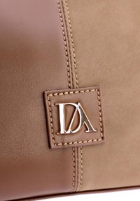 Bolso de cuero marrón con acentos cosidos y una placa rectangular con logotipo en tono plateado. Textura suave con un acabado pulido.