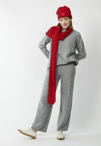 Pull en tricot gris et pantalon large associés à une �écharpe et un bonnet rouges à côtes. Des baskets blanches avec des accents beiges complètent la tenue.