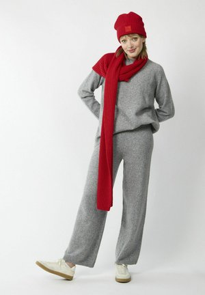 Pull en tricot gris et pantalon large associés à une écharpe et un bonnet rouges à côtes. Des baskets blanches avec des accents beiges complètent la tenue.