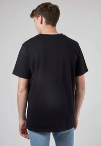 T-shirt en coton noir à manches courtes, col rond et coupe décontractée. Texture lisse avec un design simple, sans motifs ni accents visibles.