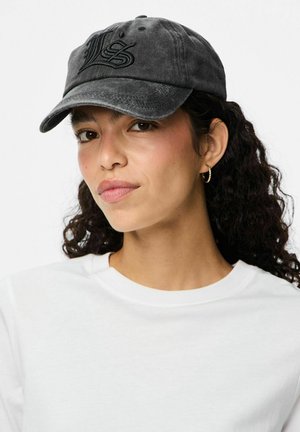 Black denim cap with embroidered logo, curved brim, and six ventilation holes. Worn with a white crew neck shirt.