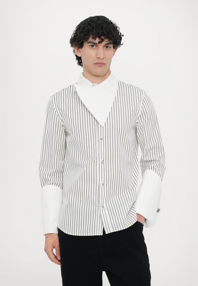 Camicia a righe bianche e nere, con un collare angolare unico, maniche a cannello e un fit sartoriale con bottoni visibili.