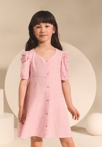 Rosa klänning med blommönster, puff�ärmar, knäppning och A-linjeformad siluett. Mjukt tyg med ett tunt blomstertryck. Slät textur.