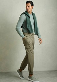 Pulover verde deschis stratificat peste un tricou gri cu mânecă lungă, asortat cu pantaloni cargo bej și adidași gri deschis. Stil casual, croială relaxată.