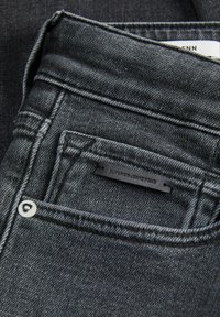 Jeans de mezclilla negra con una textura suave, que presentan costuras en tono, un bolsillo delantero y una etiqueta en el bolsillo trasero que dice "Superior Jeanswear."