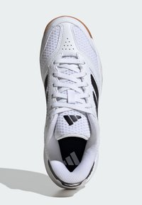 Chaussure de sport blanche avec une tige en maille, semelle en caoutchouc, accents noirs et détails perforés au niveau des orteils. Marque affichée sur la languette.