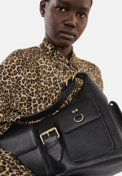 Borsa a spalla in pelle nera con superficie texture, hardware dorato, tasca frontale e tracolla ampia. La borsa è appoggiata su una camicia con stampa leopardata.