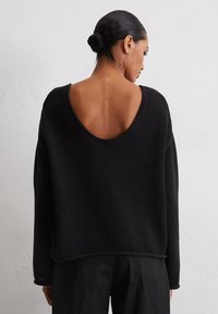 Pull en tricot noir avec un dos large en scoop, des manches longues et une coupe décontractée. Tissu texturé avec des accents côtelés à l'ourlet et aux poignets.