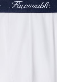 Tela blanca con una cinturilla azul marino que presenta el texto cursivo en blanco "Façonnable" en la banda.