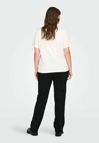 Valkoinen lyhythihainen t-paita yhdistettynä mustiin suoriin housuihin, joissa on sileät pinnat ja yksinkertaiset linjat, nähtynä takaa.