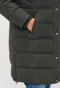 Tume roheline puhvjakks, millel on horisontaalne tikandimuster, varustatud lukuga küljetaskuga ja soonikkoes mansettidega, kinnitatud metallnuppudega.