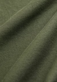 Tissu vert olive avec une texture lisse, affichant un léger éclat. Le matériau présente de douces plis et un motif de tissage fin.