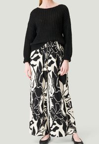 Pull en tricot noir associé à un pantalon plissé large à motifs floraux noir et blanc. Des chaussures plates noires complètent l'ensemble.