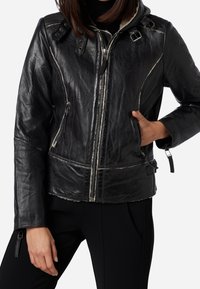 Giacca in pelle nera con zip frontale, cappuccio e tasche multiple. Presenta cuciture a contrasto e una finitura texturizzata.