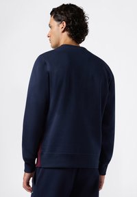 Felpa navy con scollatura rotonda, maniche lunghe e una vestibilità leggermente rilassata. Presenta dettagli laterali color bordeaux e un tessuto morbido al tatto.