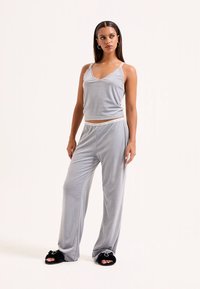 Conjunto cinza de roupa de lazer com top sem mangas com acabamento em renda e calças leves combinando. O tecido tem uma textura suave. Chinelos pretos felpudos.