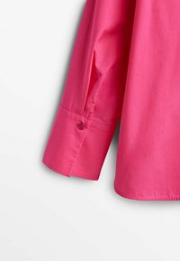 Poignet de chemise à manches longues rose vif avec un seul bouton sur un fond clair uni.