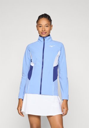 Chaqueta deportiva de color azul claro con un alto cuello, cremallera, detalles en azul marino y paneles laterales blancos. Tejido suave, mangas largas y diseño ajustado.