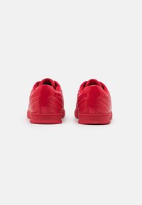Rote Sneaker mit einem schlanken Design, glänzender Oberfläche, strukturierten Akzenten und gepolstertem Kragen. Die Sohle ist flach und hat eine glatte Oberfläche.