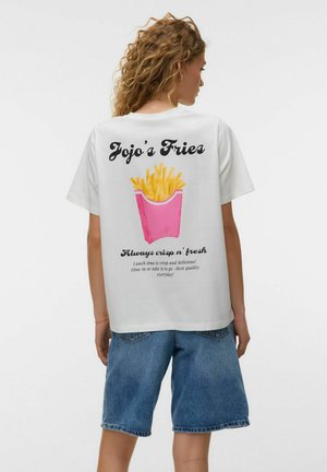 Junge Frau mit lockigem Haar, die ein weißes T-Shirt mit einer pinkfarbenen Pommes-Schachtel und der Aufschrift „Jojo's Fries“ auf dem Rücken trägt, kombiniert mit Jeans-Shorts.