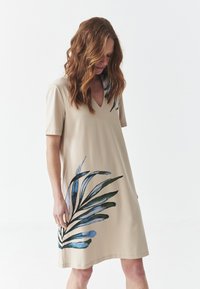 Abito beige a maniche corte con scollo a V, caratterizzato da un design di foglie blu e verdi sulla parte anteriore. Tessuto morbido con una vestibilità rilassata e cuciture minime.