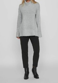Grauer, strukturierter Pullover mit hochabschließendem Kragen, langen Ärmeln und rohem Saum, kombiniert mit schwarzen, schmalen Hosen und eleganten, schwarzen Ankle Boots.