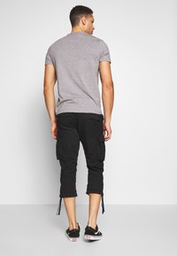 Grijs kortearmsgem t-shirt, gecombineerd met zwarte cargobroek met dijzakken en verstelbare boorden, gedragen met zwarte sneakers.