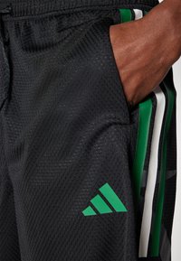 Black athletic shorts with a textured mesh material, featuring a green Adidas logo and green and white vertical stripes on the sides.