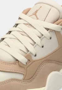 Gros plan d'une basket beige et crème avec des lacets texturés, des panneaux en daim et en cuir, et un logo Jumpman sur la languette.