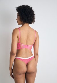 Pink lace lingerie set featuring a strappy back design and elastic accents. The thong has a white waistband and intricate lace detailing.