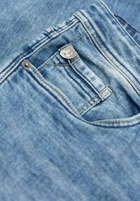 Vaqueros de mezclilla azul claro con un botón de metal plateado y detalles de costura. La tela tiene un aspecto descolorido y texturizado.