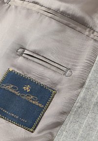 Tessuto interno grigio con una texture liscia, caratterizzato da un'etichetta cucita in blu navy e filo dorato per Brooks Brothers, e una piccola tasca.