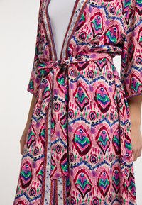Barviti kimono z vzorcem v rožnati, zeleni in modri barvi. Ima pas za zavezovanje, polovične rokave in okrasne kovinske detajle ob robovih.