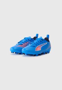 Botas de fútbol sintéticas azules con una superficie texturizada, detalles en naranja, cordones planos, tacos de goma y una lengüeta en el talón.