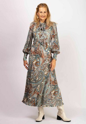 Langes, mit Paisleymuster in Blau-, Braun- und Cremetönen; mit einer Krawatten-Neckline und puffigen langen Ärmeln. Kombiniert mit weißen Knöchelstiefeln.