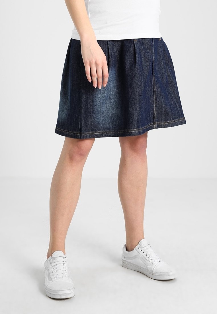 Falda de mezclilla en azul oscuro, con un diseño acampanado, plisados y costuras en contraste. Combinada con zapatillas blancas.