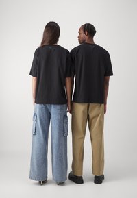 Black t-shirts with a relaxed fit, worn with light blue cargo and khaki pants, showcasing diverse textures and styles.
