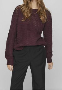 Mörk vinröd stickad tröja med ett texturerat mönster, ribbade ärmmuddar och lös passform, tillsammans med svarta byxor.