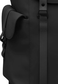 Zaino nero con finitura opaca, dotato di tasca a patta, cinturino regolabile e cuciture piatte. Linee pulite e design minimalista.