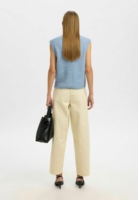 Mėlynas megztas be rankovių viršus, kreminės plačios kelnes ir juoda rankinė. Glotni tekstūra, laisvas siluetas, su smailiais juodais aukštakulniais.