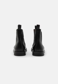Botas de cuero negras hasta el tobillo con paneles laterales elásticos, suela plana y lengüetas en la parte trasera. Textura suave y diseño minimalista.