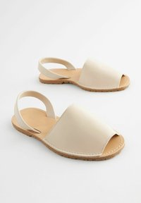 Sandali in pelle beige con punta aperta, cinturini regolabili alla caviglia e suola in gomma marrone chiaro con un motivo testurizzato.