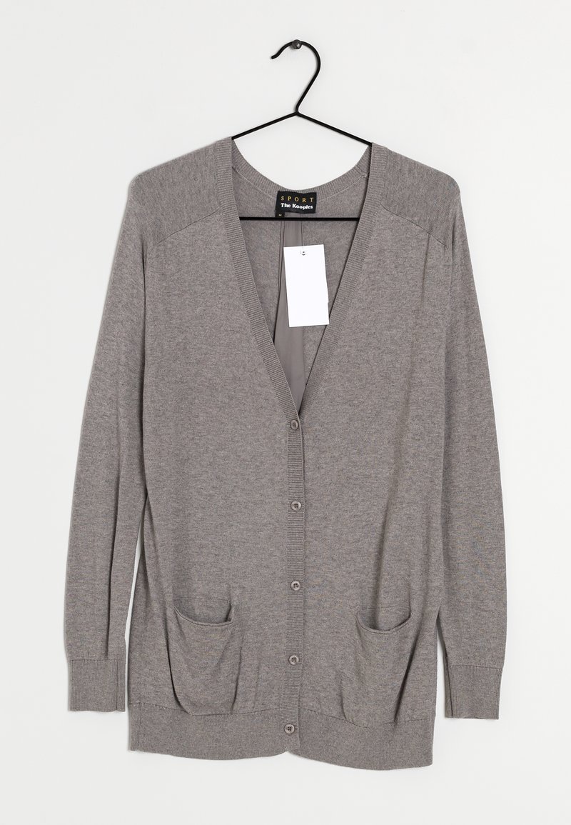 Harmaa neuletakki v-pääntällä, pitkillä hihoilla ja napp closurella. Sisältää kaksi etutaskua ja ripustettavan lipukkeen.