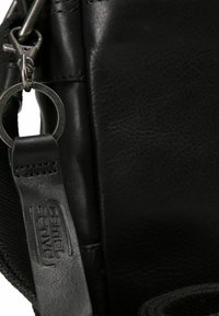 Bolso de cuero negro con superficie texturizada, herrajes de plata, un enganche para llavero de metal y una etiqueta de cuero con marca.
