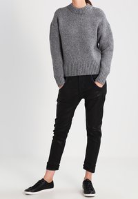 Šedý pletený svetr s kulatým výstřihem, černé slim-fit kalhoty a černé tenisky. Textura svetru je hrubá a teplá.