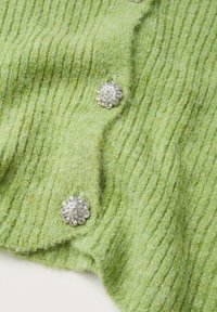 Grüner gerippter Strickstoff mit weicher Textur, versehen mit silbernen, blütenförmigen Knöpfen, die mit klaren Kristallen verziert sind.