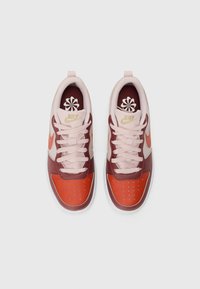 Nike tenisice s tamnocrvenom i narančastom bojom, glatkim kožnim materijalom, ružičastim vezicama i cvjetnim logotipom na jeziku.