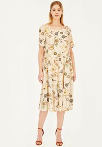 Sukienka z krótkim rękawem, sięgająca do kolan w jasnym beżu, z wielokolorowym nadrukiem różnych obiektów, z rozkloszowanym dołem i subtelną teksturą.
